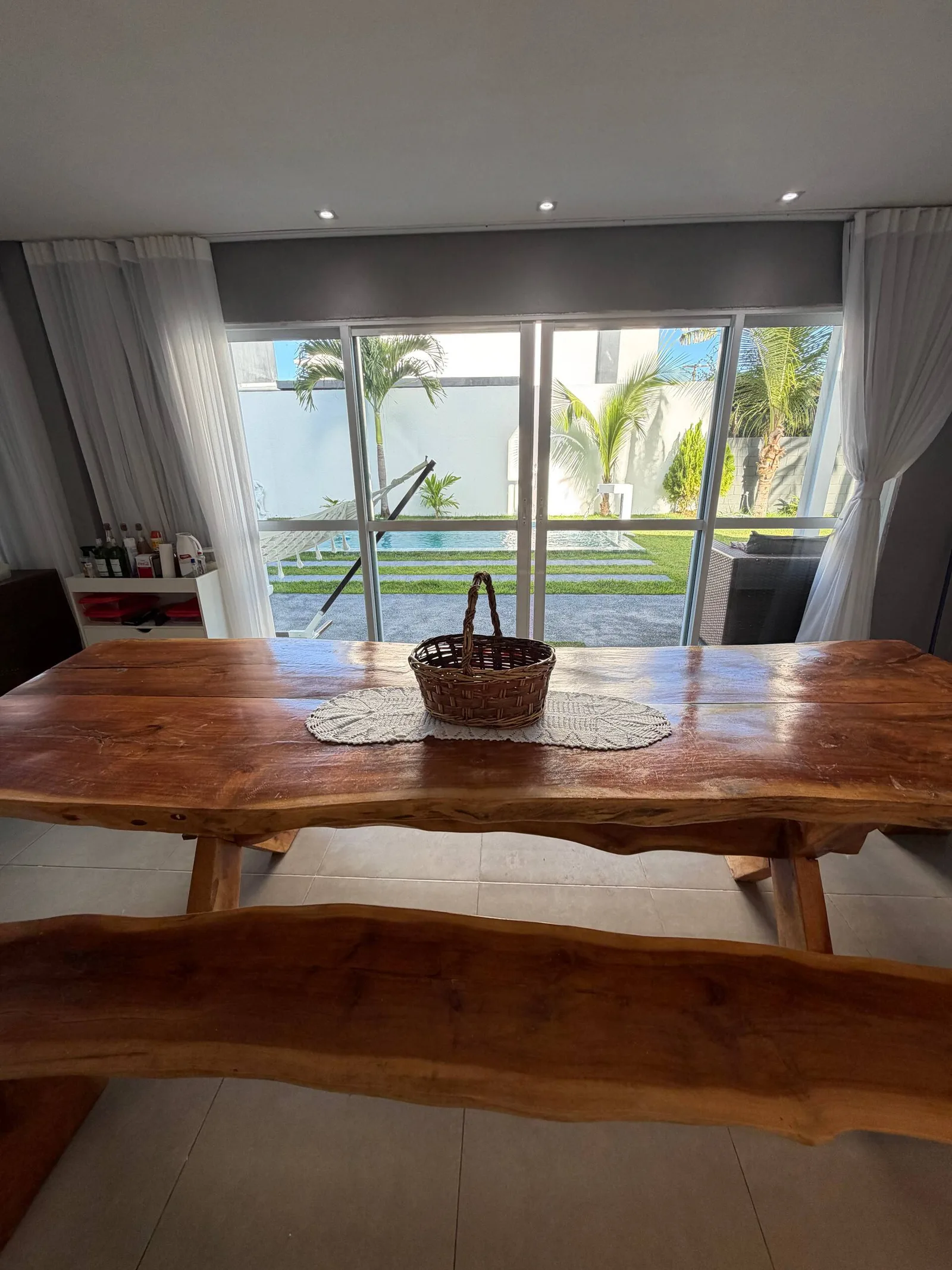 Mesa de madeira maciça posta, cozinha gourmet ao fundo com portas de vidro