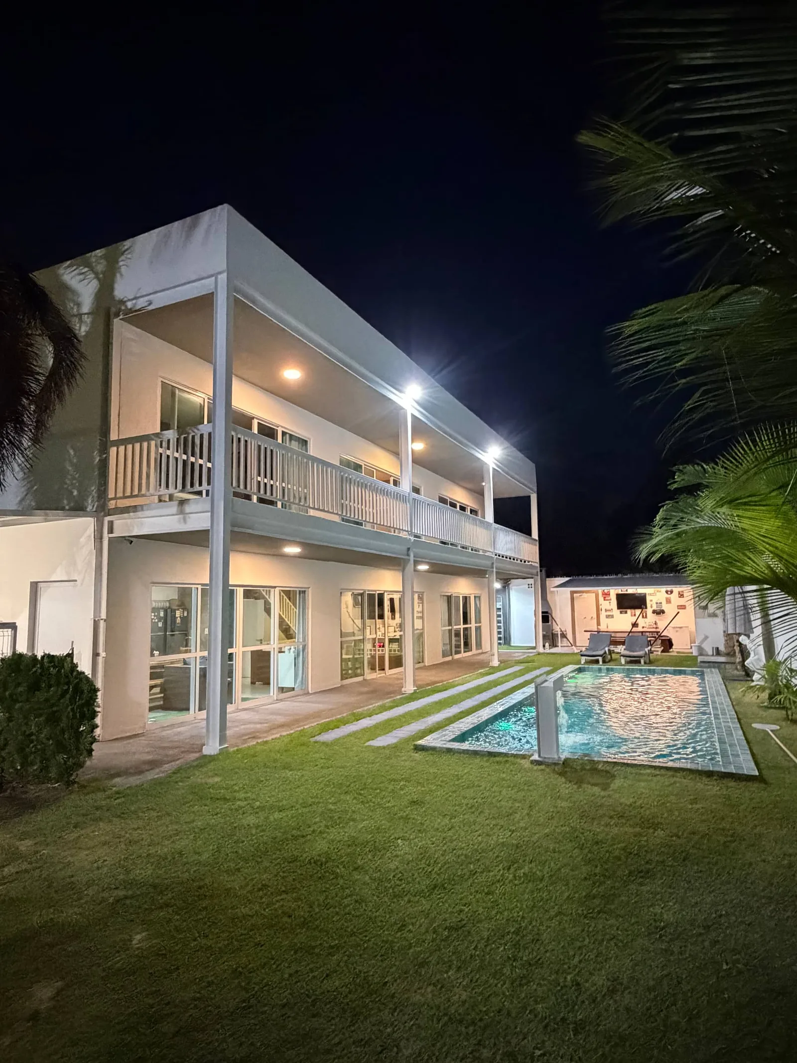 Casa e piscina à noite, luz das varandas refletida na água
