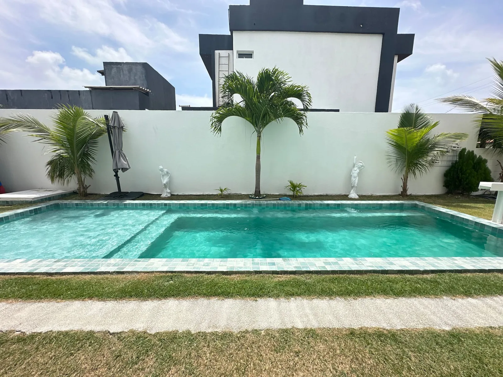 Piscina com jatos de hidromassagem ativos, pastilha turquesa e grama ao redor