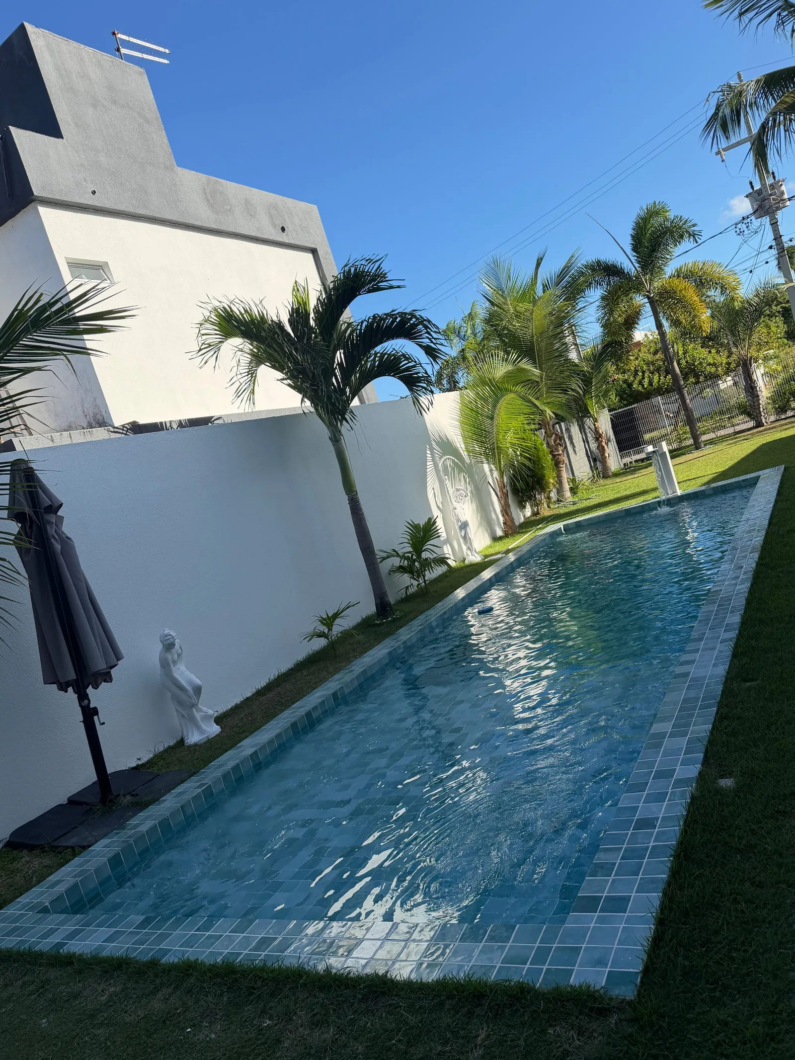 Muro branco, coqueiros e piscina vistos do segundo pavimento