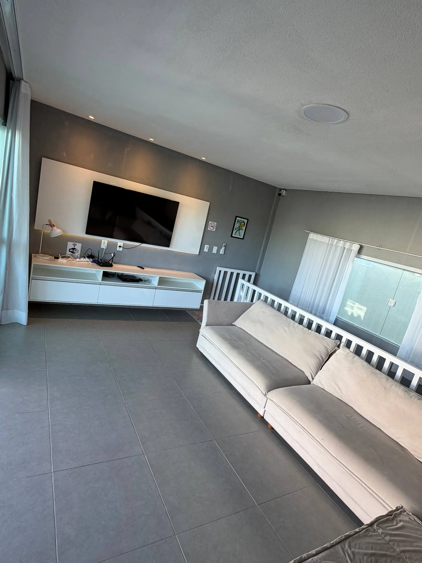 Sala de estar com sofá branco, TV de painel e piso em porcelanato